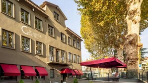 Een boetiekhotel met een klassiek gevelontwerp, terras en een grote boom die schaduw biedt.