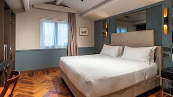 Un dormitorio con una cama grande, piso de madera, ventana con cortinas, espejo y una lámpara de pared.