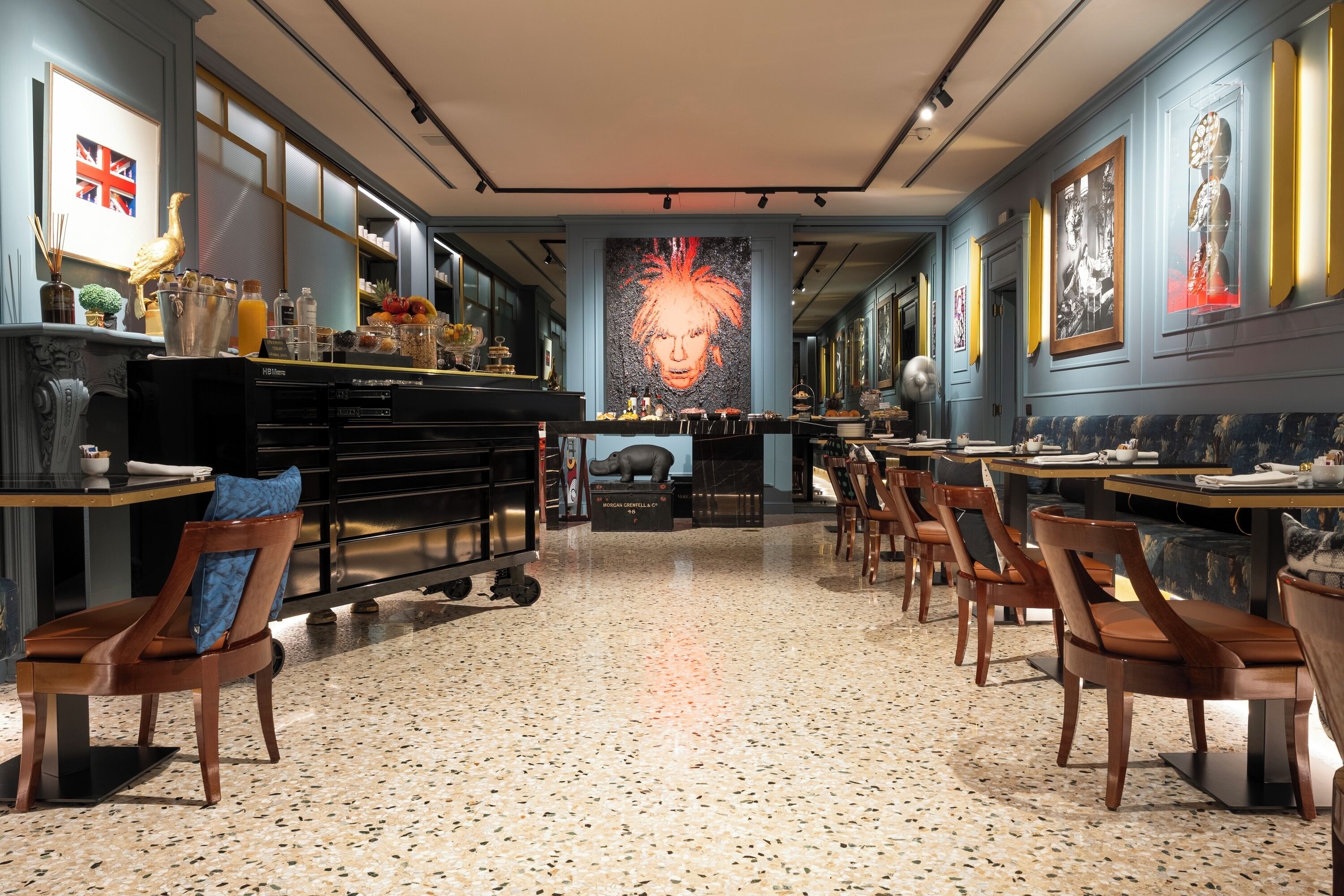 A restaurant with a long counter, wooden chairs, and a large mural on the wall.