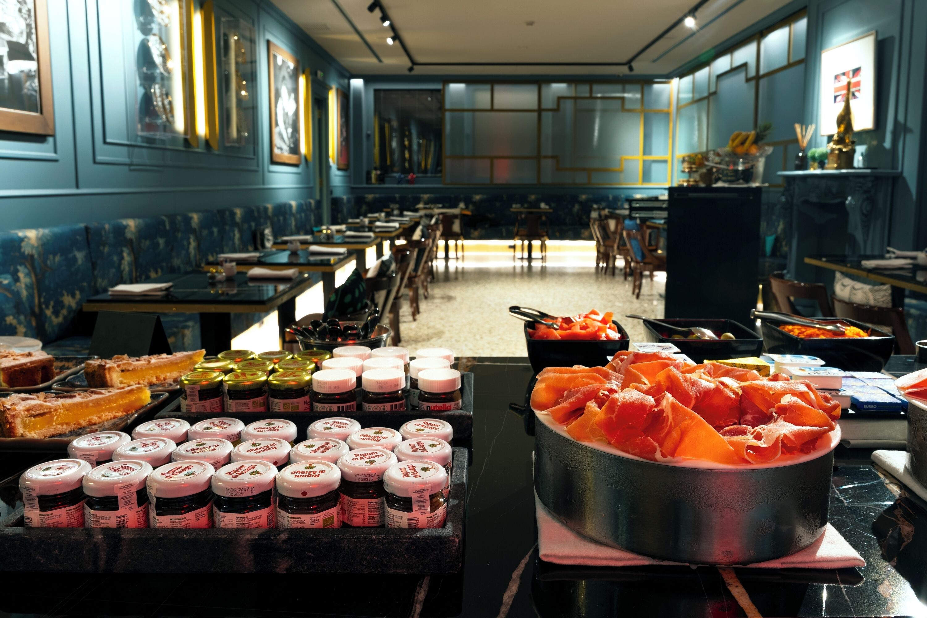 A restaurant with long communal tables, a buffet with various food items, and a large pot of food in the center.