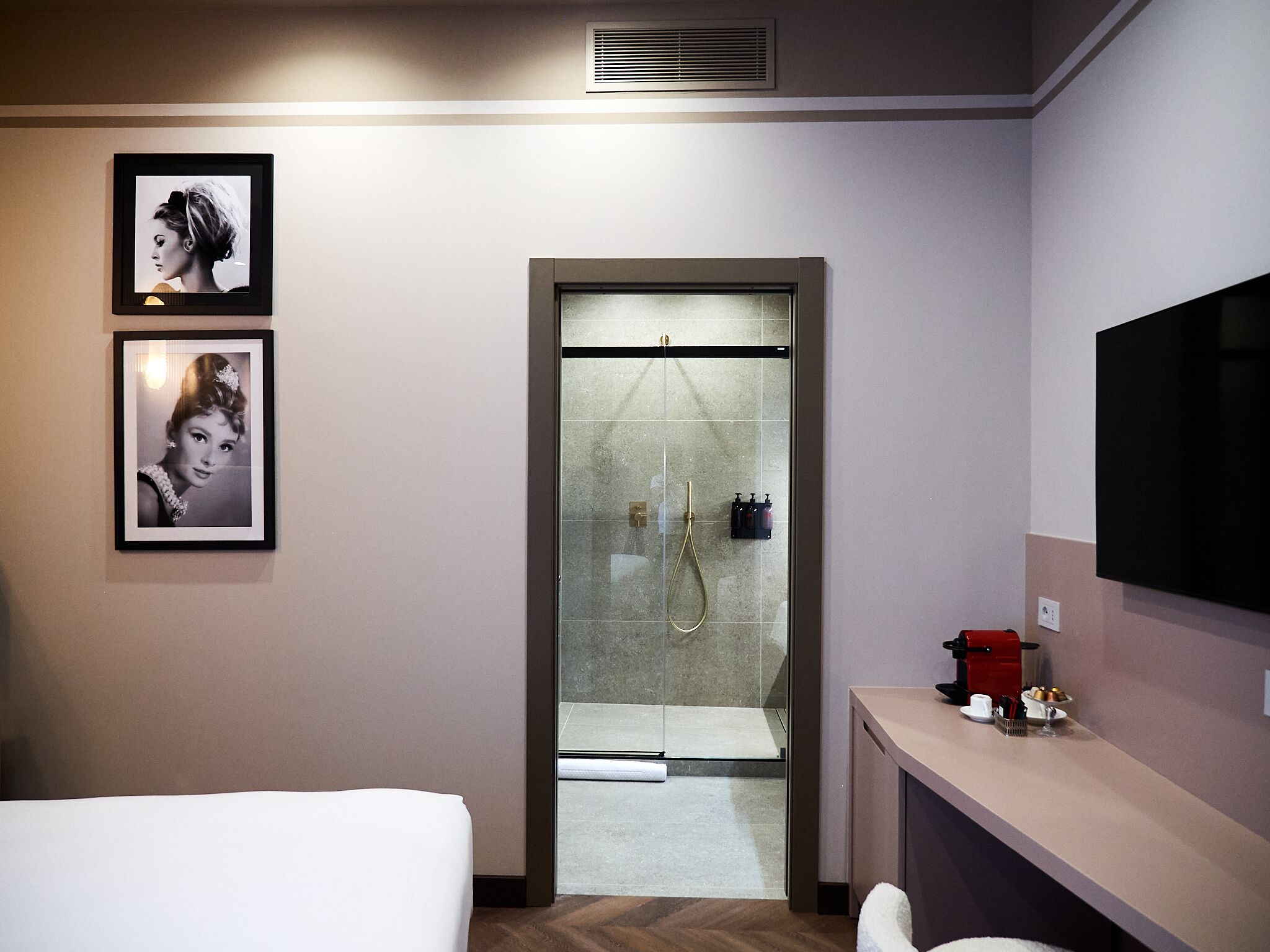 Una habitación de hotel moderna con una cama, un escritorio con cafetera y una zona de ducha.