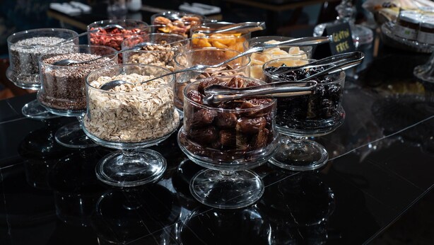 Een buffet met verschillende soorten eten in glazen schalen, zoals granen, noten en gedroogd fruit.