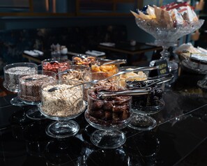 Ein Buffet mit verschiedenen Speisen in durchsichtigen Glasbehältern, darunter Getreide, Nüsse und Trockenfrüchte.