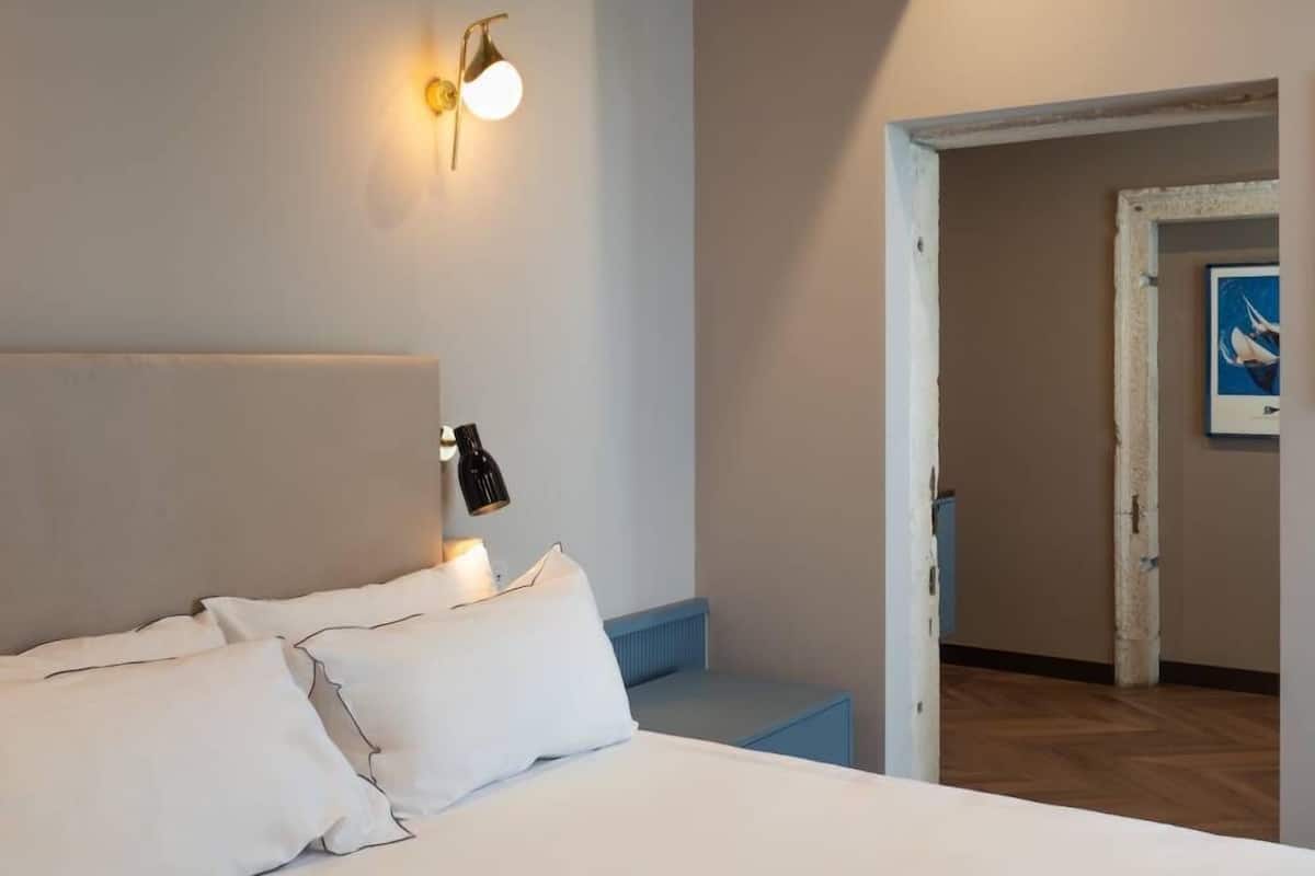 Une chambre à coucher avec un lit, deux lampes fixées au mur, une porte donnant sur une autre pièce et un tableau encadré accroché au mur.
