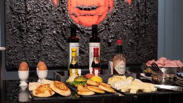 A buffet table with various food items, including eggs, bread, and meats, set against a textured wall with a large portrait.