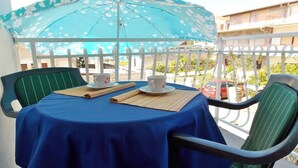 A balcony with a table covered by a blue tablecloth, two chairs, a blue umbrella, and a white fence. - Bakmaz Apartment (Vodice)
