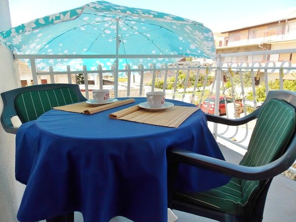 A balcony with a table covered by a blue tablecloth, two chairs, a blue umbrella, and a white fence. - Bakmaz Apartment (Vodice)