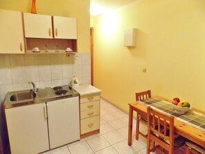 A compact kitchen with a sink, stove, and cabinets, a dining table with chairs, and a bowl of fruit on the table. - Bakmaz Apartment (Vodice)