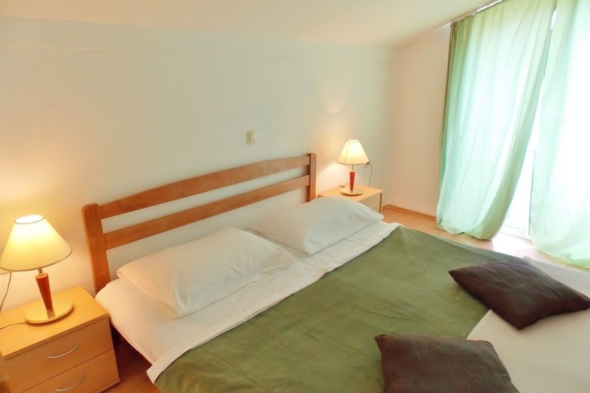 A neatly made bed with a green bedspread and white pillows, two bedside lamps, and a wooden nightstand with drawers.