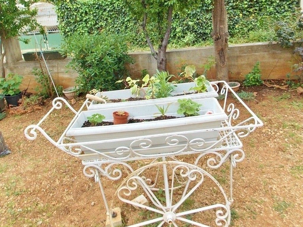 Een witte metalen tuinschaar met twee rechthoekige plantenbakken met diverse planten.