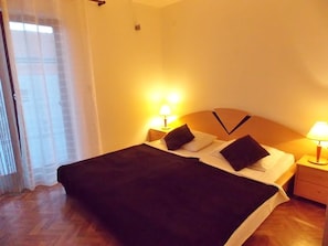 A hotel room with a bed, two bedside lamps, a wooden headboard, and a window with sheer curtains. - Bakmaz Apartment (Vodice)
