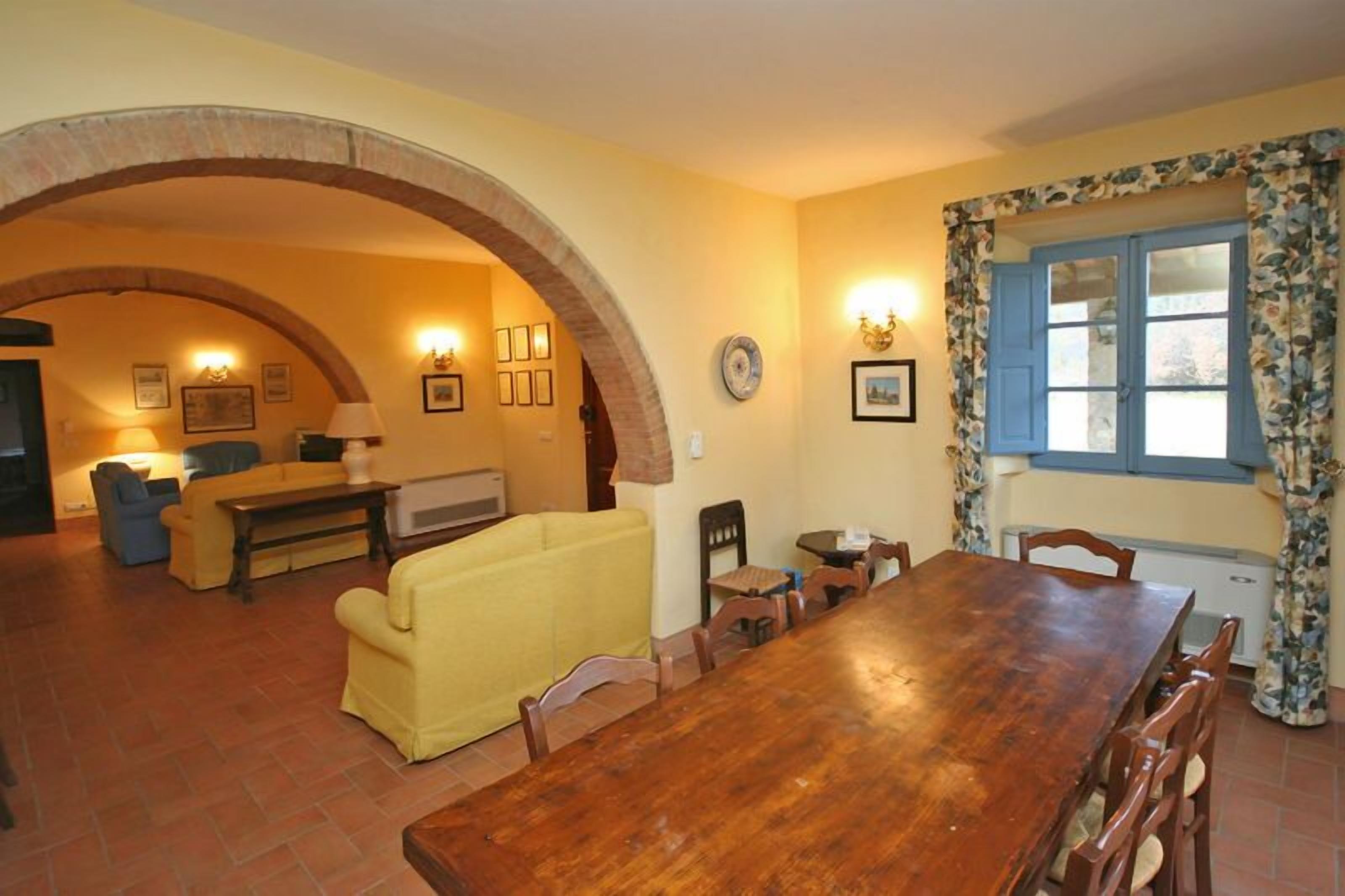 Un coin repas avec une table et des chaises en bois, un canapé jaune et une arche en briques.