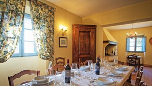 A dining room with a long table set for a meal, wooden chairs, a chandelier, and a fireplace. - Villa Sodi (Castellina in Chianti)