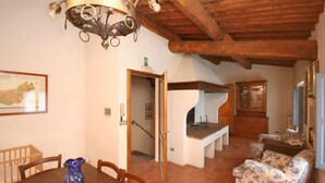 A dining area with a wooden table, chairs, a blue vase, a chandelier, and a fireplace. - Villa Sodi (Castellina in Chianti)