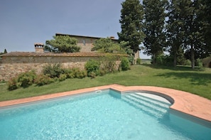 A swimming pool with a stone wall and greenery in the background.