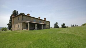 A rustic stone house with a sloped roof, a covered porch, and a grassy lawn. - Villa Sodi (Castellina in Chianti)