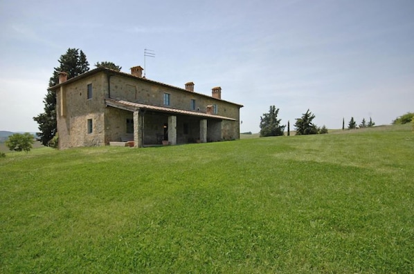 A rustic stone house with a sloped roof, a covered porch, and a grassy lawn.