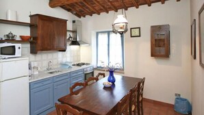 A kitchen with wooden cabinets, a white refrigerator, a microwave, and a dining table with chairs. - Villa Sodi (Castellina in Chianti)
