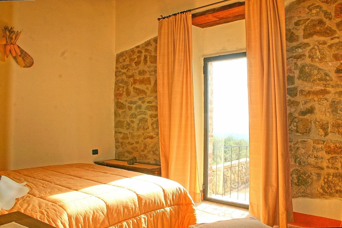 Ein Schlafzimmer mit einer Steinswand, einem Bett mit weißem Kopfkissen und einem Fenster mit Vorhängen.