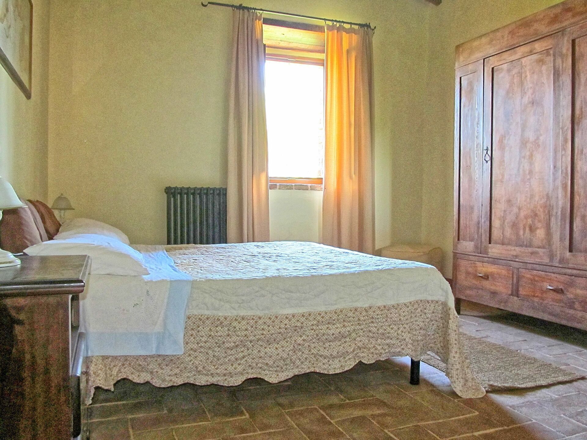 A bedroom with a bed, a wooden wardrobe, a radiator, and a window with curtains.