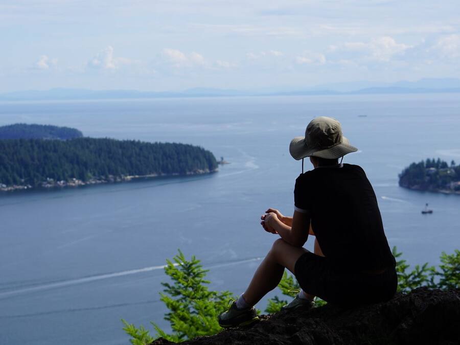 A person sitting on a rock overlooking a large body of water with a forested island in the distance.