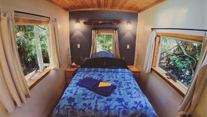Une chambre à coucher avec un lit, deux fenêtres et une vue sur les arbres.