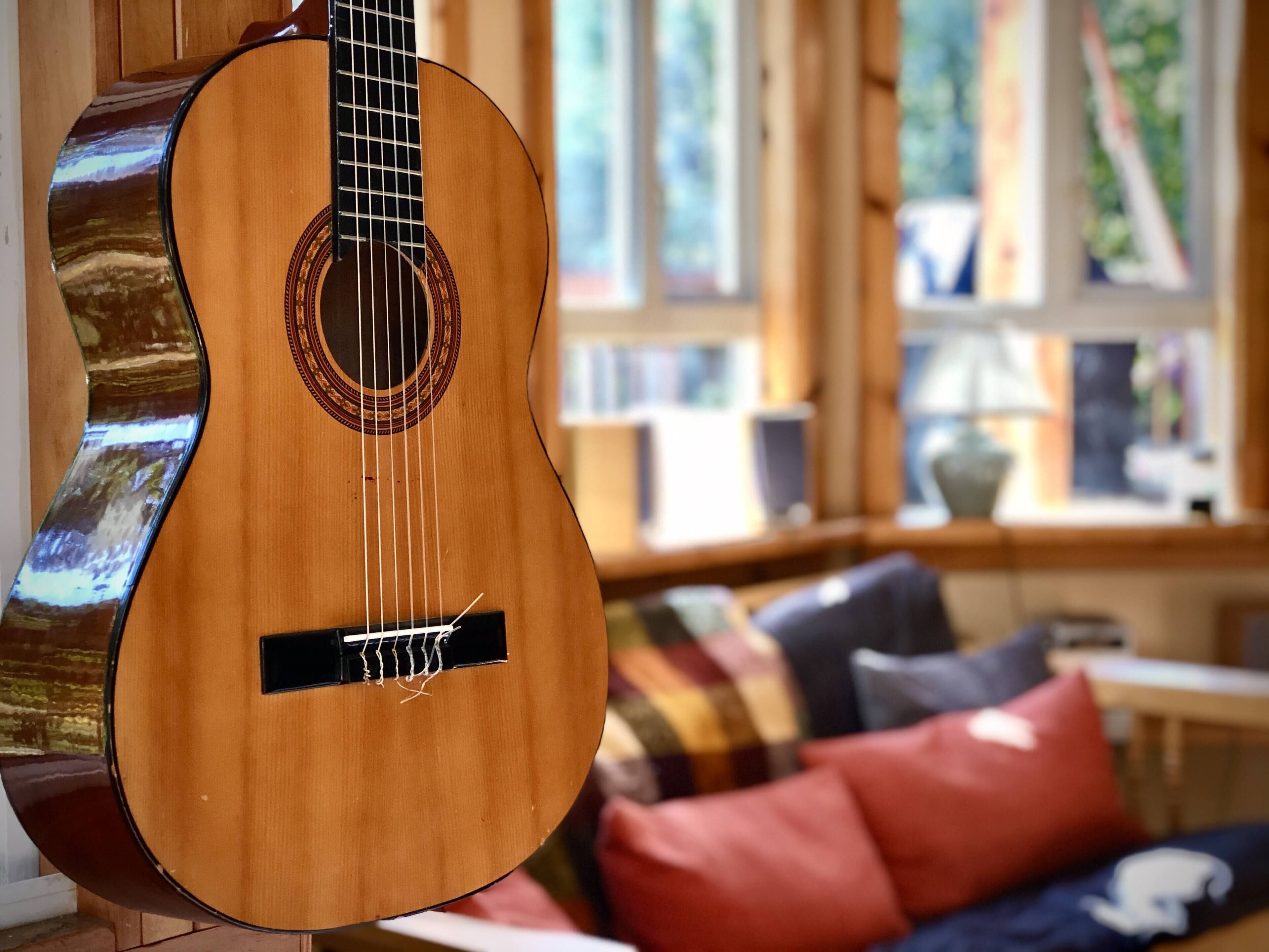Una chitarra appesa al muro in una stanza con una finestra, un divano con dei cuscini e un tavolino.