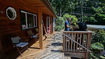 Une cabane en bois dotée d’une véranda, d’un espace salon extérieur et d’un coin barbecue.