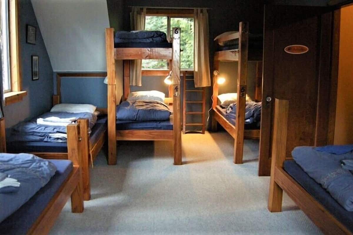 Een slaapzaal met stapelbedden, een trapje en een raam met gordijnen.