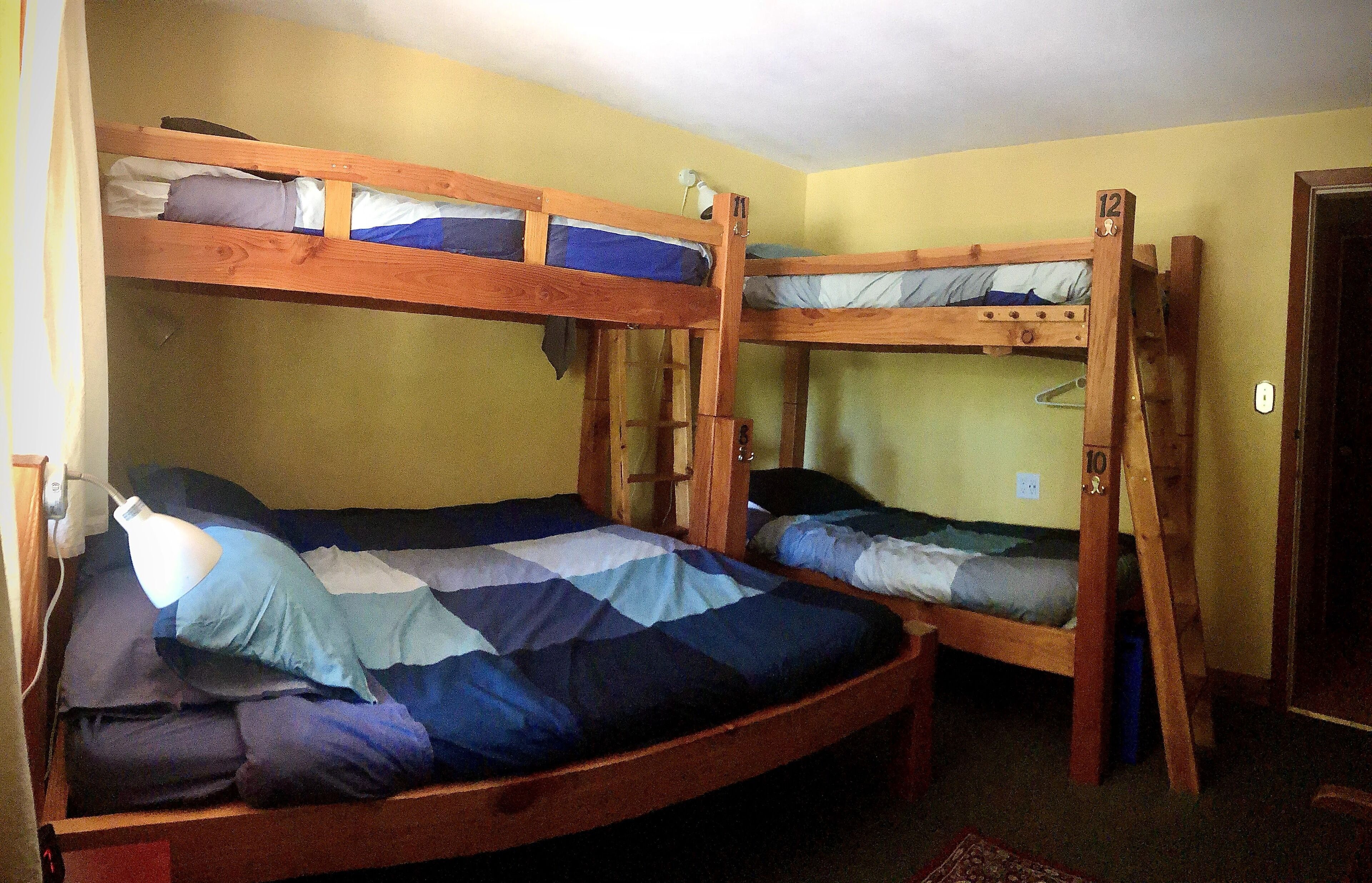 Une chambre avec deux lits superposés, chacun doté d’une structure en bois et d’un matelas. On trouve une petite table et une lampe sur l’un des lits.