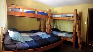 Une chambre avec deux lits superposés, chacun doté d’une structure en bois et d’un matelas. On trouve une petite table et une lampe sur l’un des lits.