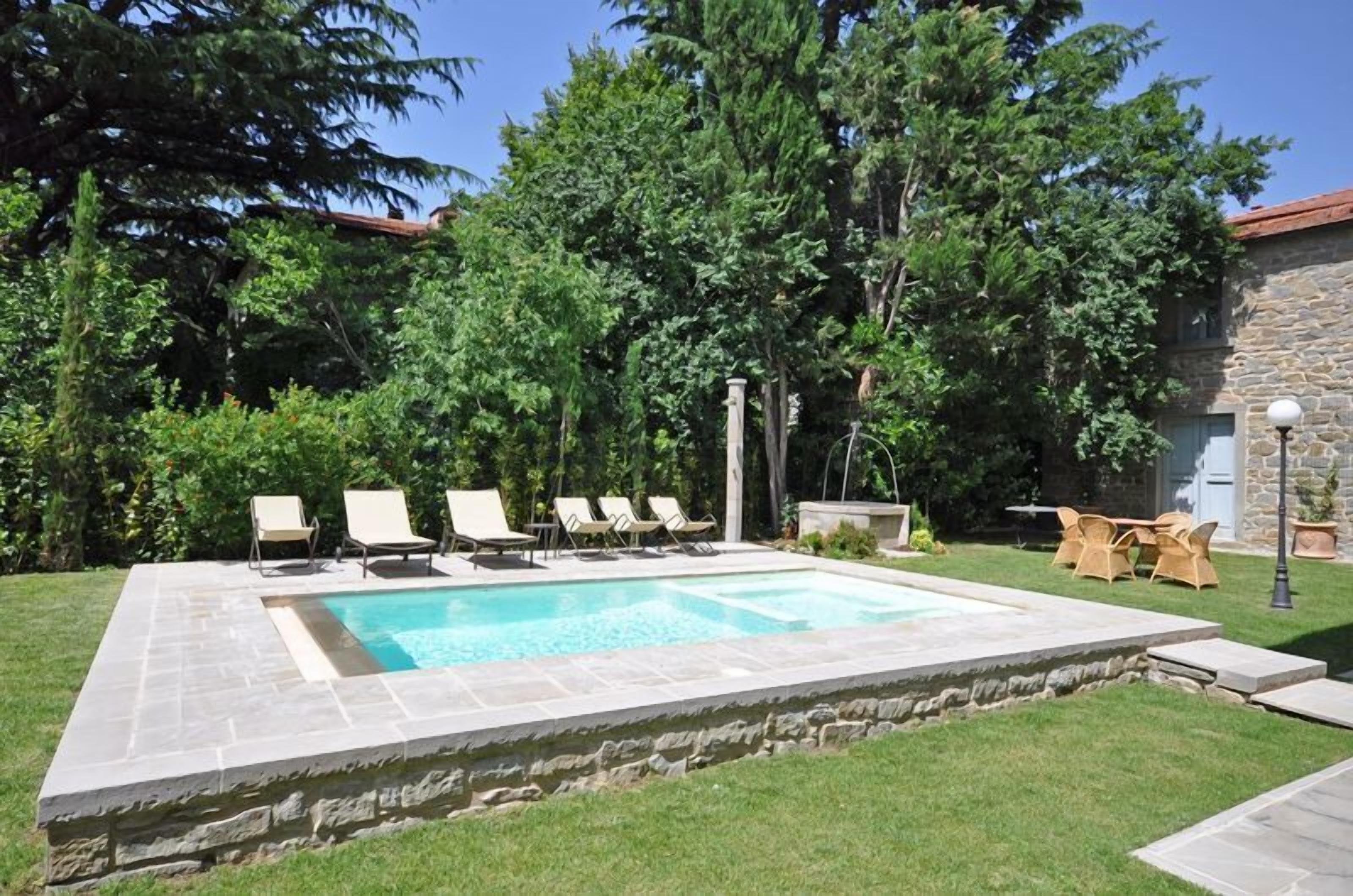 A rectangular swimming pool with a stone border, surrounded by a grassy lawn and trees.