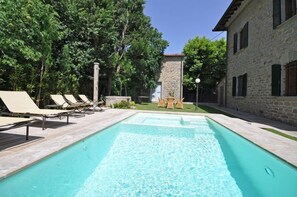 Una piscina con sillas de descanso y un edificio de piedra al fondo.