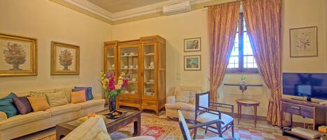 Uma sala de estar com sofá, poltronas, mesa de centro, aparador e televisão.