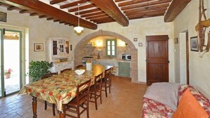 Un comedor rústico con una mesa y sillas de madera, un arco que da a una cocina y una zona de estar acogedora con un sofá.
