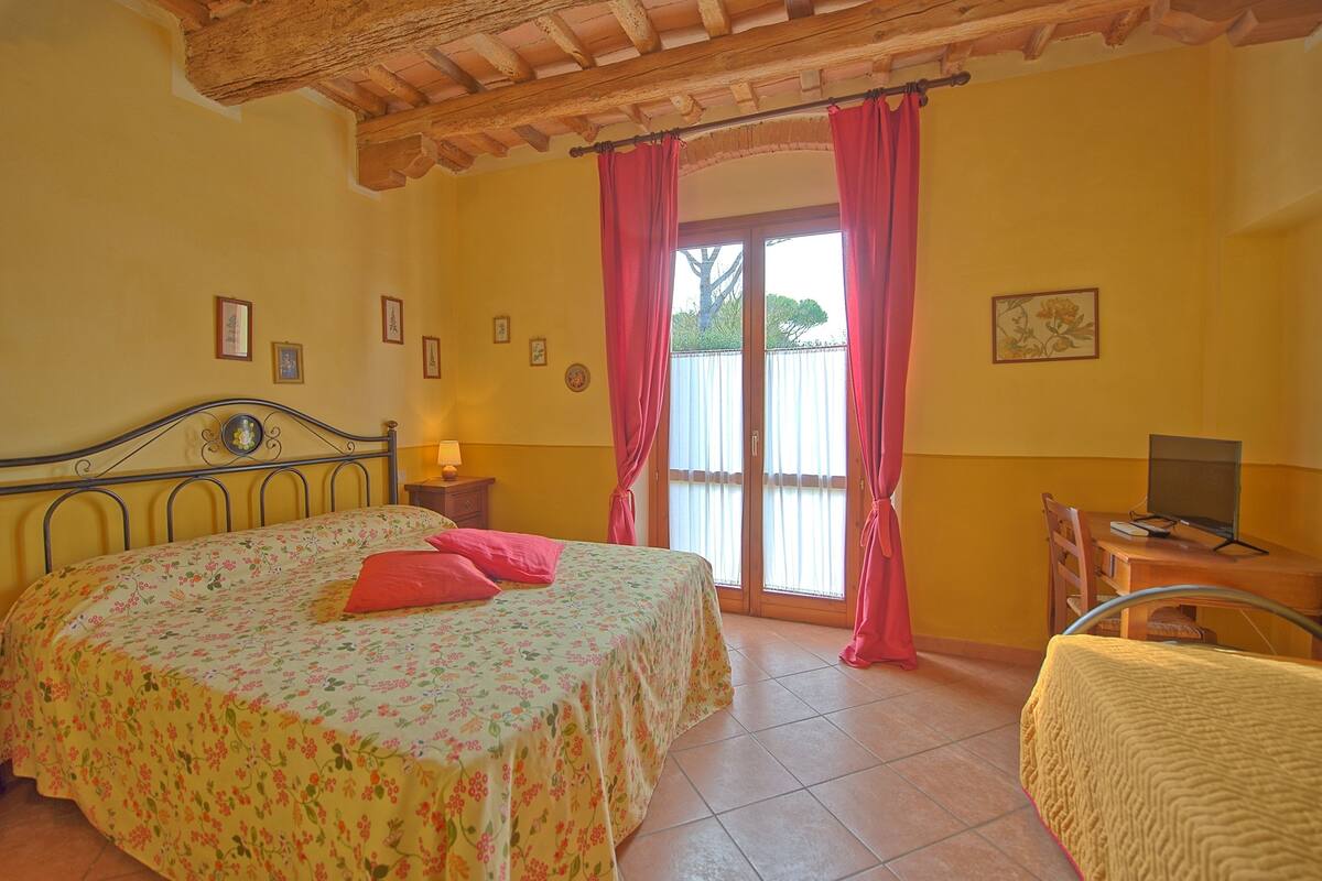 Un dormitorio con cama, escritorio, silla, televisión y ventana con cortinas.