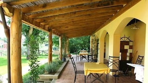 Une terrasse extérieure avec des poutres en bois, des carreaux de terre cuite et une table recouverte d’une nappe jaune.