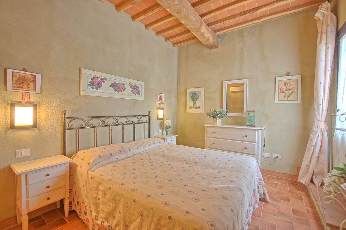 Un dormitorio con cama, mesitas de noche, cómoda, espejo e iluminación en la pared.