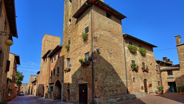 A narrow street with historic buildings, including a prominent tower with arched windows and a door. - Certaldo (Certaldo)