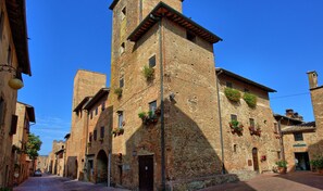 A narrow street with historic buildings, including a prominent tower with arched windows and a door. - Certaldo (Certaldo)