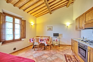 A kitchen with wooden cabinets, a dining table with chairs, a TV on a stand, and a window with curtains. - Certaldo (Certaldo)