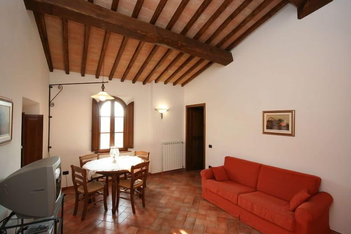 A dining area with a table and chairs, a red sofa, and a ceiling with wooden beams.