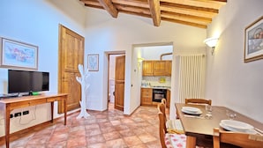 A cozy dining area with a wooden table and chairs, a television on a desk, and a kitchen in the background. - Certaldo (Certaldo)