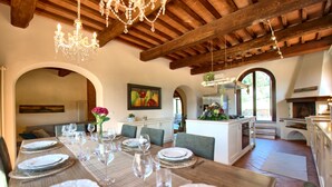 A dining area with a wooden table set for a meal, a chandelier, and a kitchen in the background. - Villa Nora (Empoli)