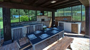 An outdoor kitchen with a stone countertop, a built-in grill, and a dining area with a table set for four. - Villa Nora (Empoli)