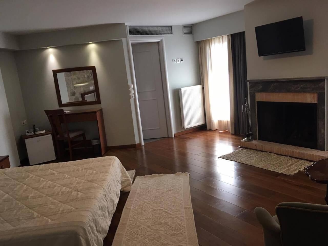 A hotel room with a bed, a desk, a chair, a fireplace, and a television.