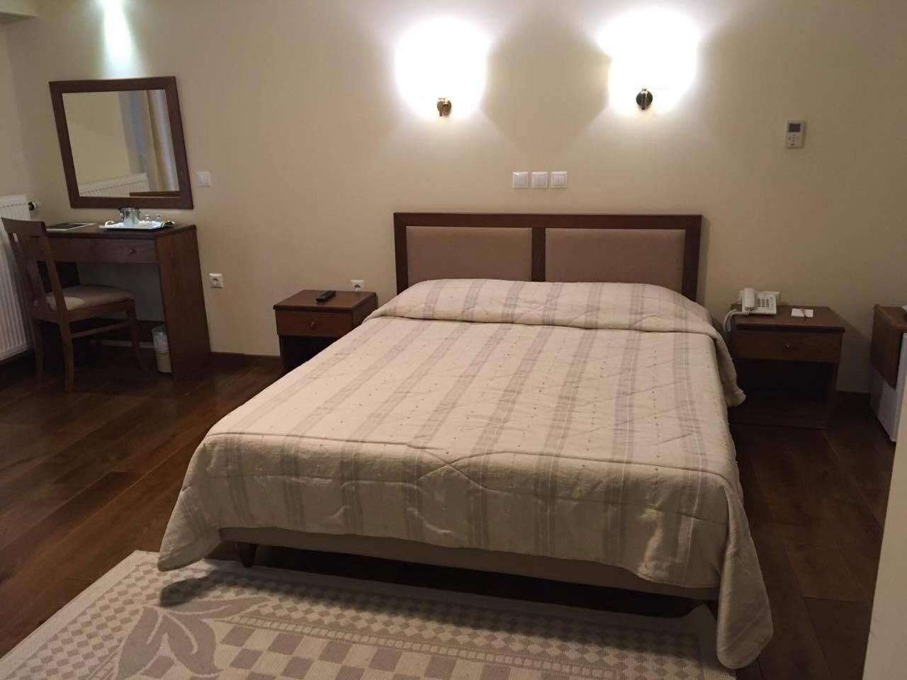 Una camera d'albergo con un letto grande, una scrivania con una sedia, due comodini e uno specchio a parete.