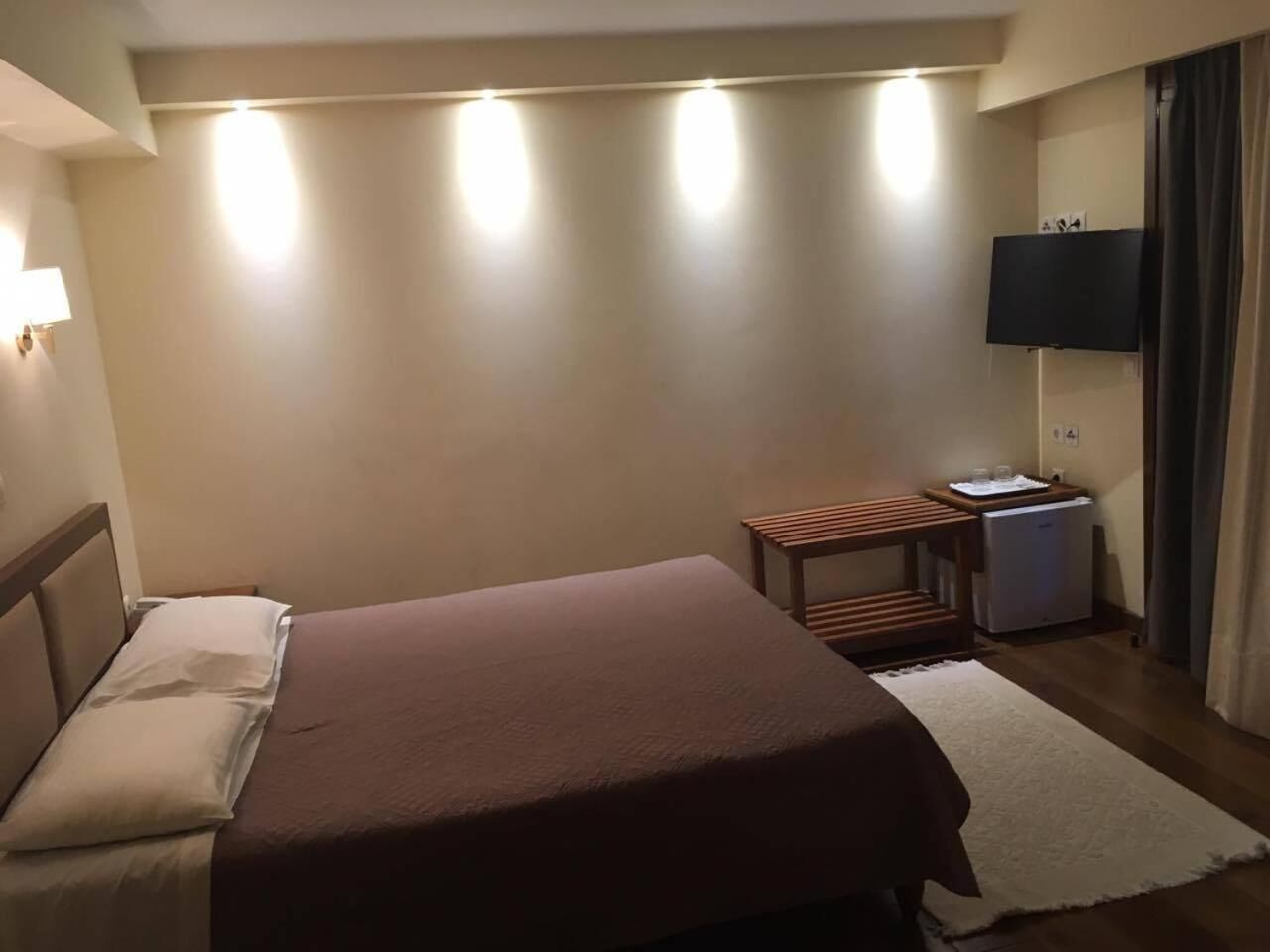 A hotel room with a bed, a small table, a TV, and a desk with a computer.