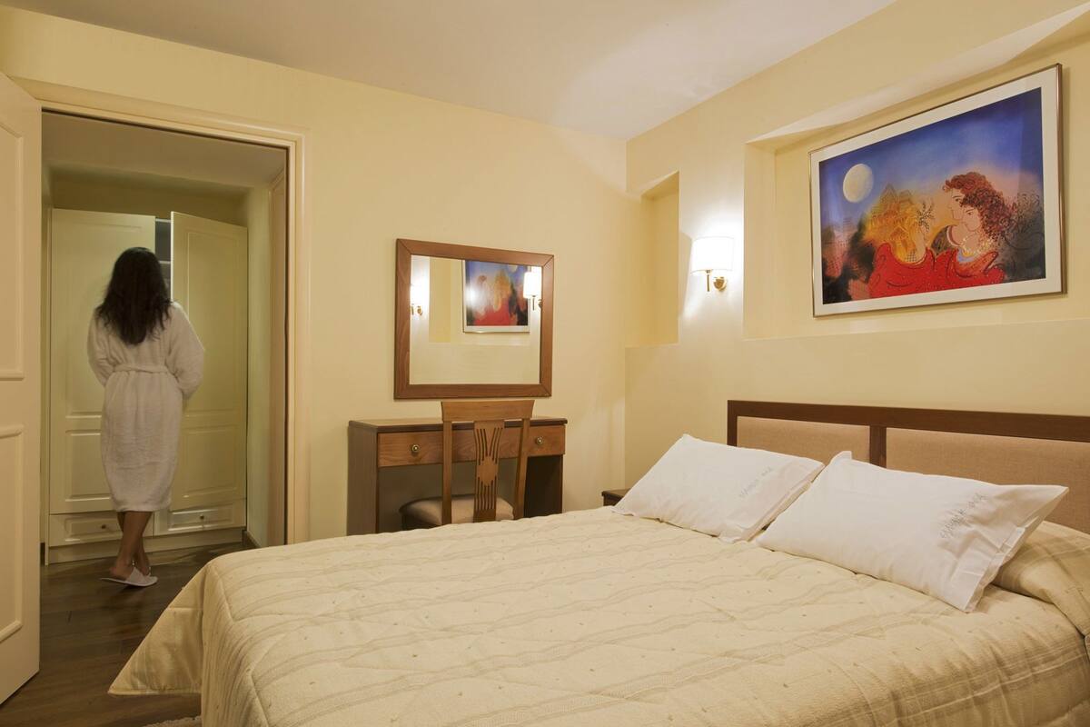 Une chambre d’hôtel comprenant un lit, un bureau, une chaise, une table de chevet, un tableau et un miroir.