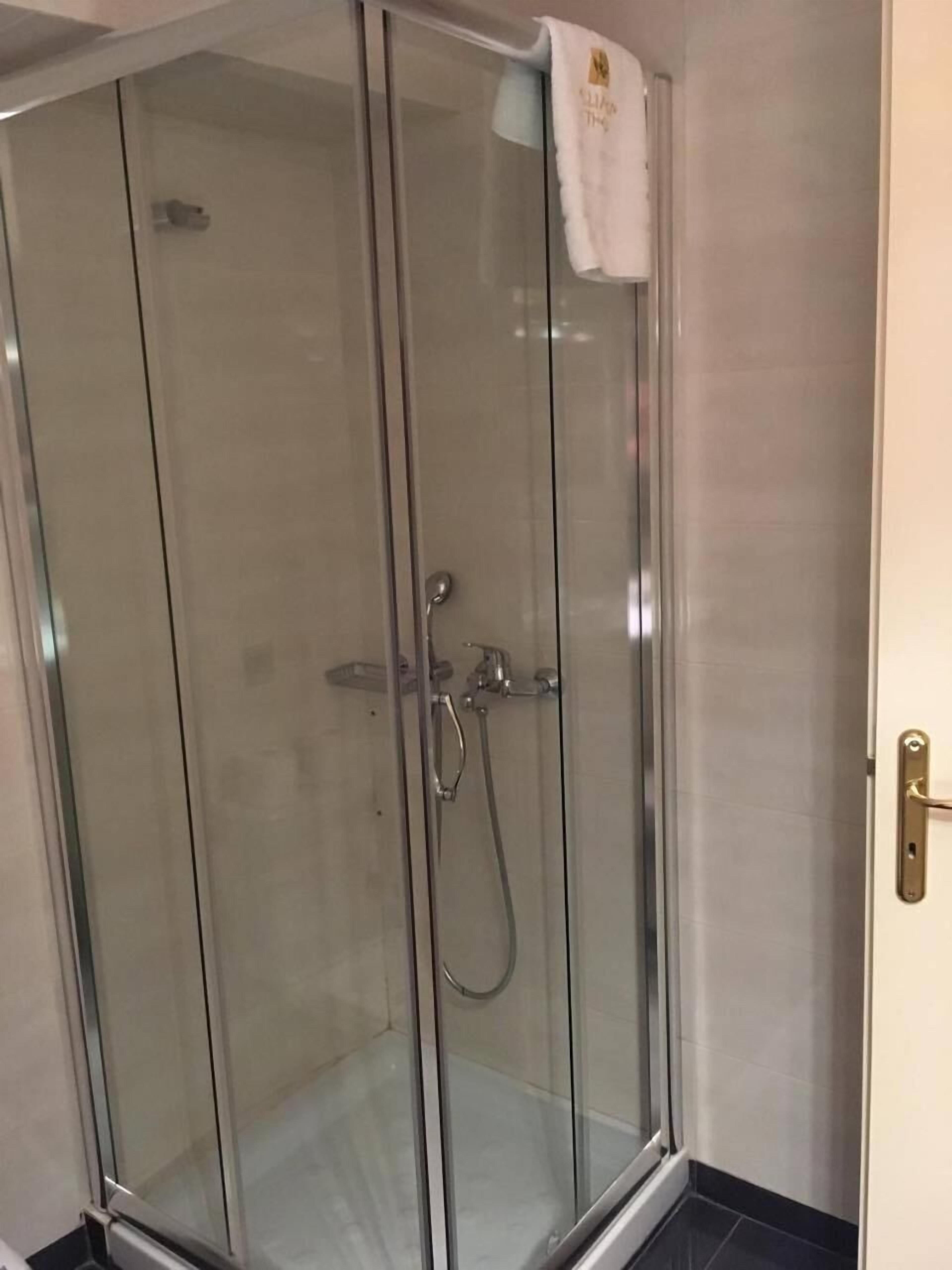 Une douche fermée par des parois en verre, avec une serviette accrochée à la poignée de la porte.
